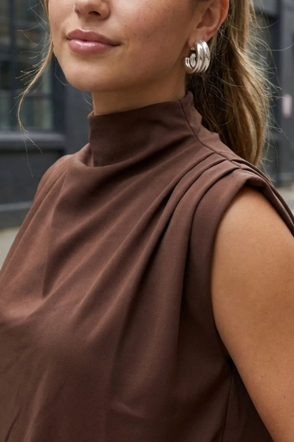Blusa de fit oversized, sin mangas y cuello alto con detalles plisados en hombros.